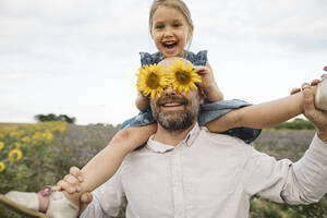 Sonnenblumen bedecken die Augen eines verspielten Mannes mit Tochter auf einem Feld - KMKF01064