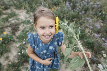 Portrait of happy girl with a sunflower in a field - KMKF01071