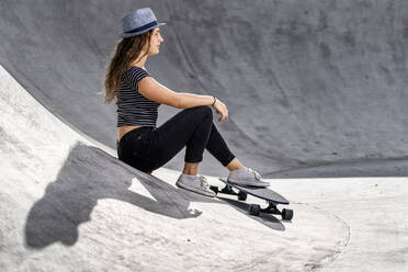 Junge Frau mit Skateboard im Skatepark sitzend - STSF02213