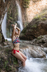 Junge Frau posiert an einem Wasserfall mit verbrannter Haut - LJF00903