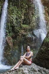 Young woman sitting at a waterfall - LJF00910