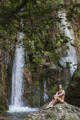 Junge Frau sitzt an einem Wasserfall - LJF00911