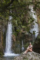 Young woman sitting at a waterfall - LJF00911