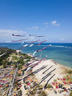 Drohnenansicht von Drachen, die während eines Festivals auf Bali, Indonesien, über dem Strand gegen den blauen Himmel fliegen - KNTF03340