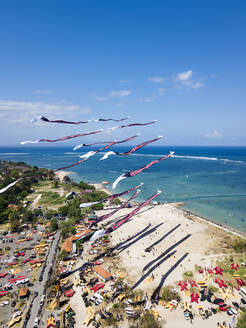 Drone view of kites flying over beach against blue sky during festival in Bali, Indonesia - KNTF03340