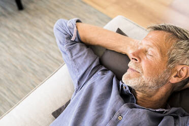 Senior man lying on couch at home taking a nap - SBOF01991