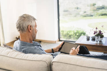 Älterer Mann benutzt Tablet auf der Couch zu Hause - SBOF01993