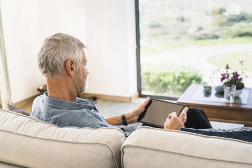 Älterer Mann benutzt Tablet auf der Couch zu Hause - SBOF01993
