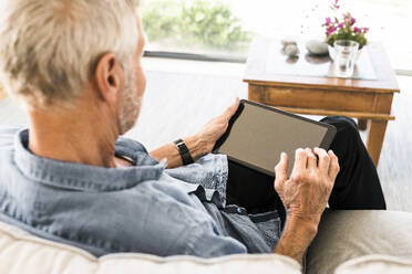Senior man using tablet on couch at home - SBOF01994
