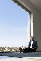 Senior businessman sitting at panorama window looking out - SBOF02002