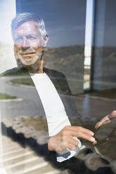 Lächelnder älterer Geschäftsmann mit Tablet am Fenster - SBOF02005