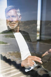 Smiling senior businessman using tablet at the window - SBOF02005