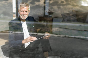 Smiling senior businessman using tablet at the window - SBOF02007