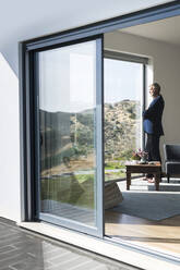 Senior businessman standing at panorama window looking out - SBOF02009