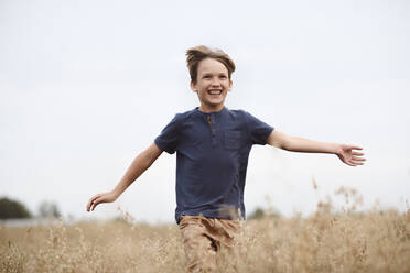 Porträt eines lachenden Jungen, der in einem Haferfeld läuft - EYAF00420