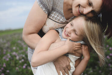 Happy grandmother hugging granddaughter on flower meadow - EYAF00421