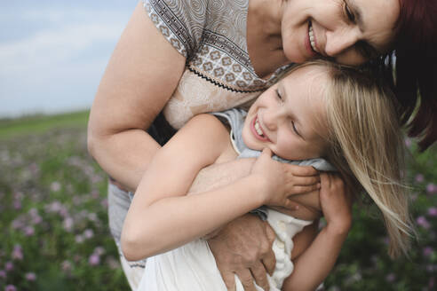 Glückliche Großmutter, die ihre Enkelin auf einer Blumenwiese umarmt - EYAF00421