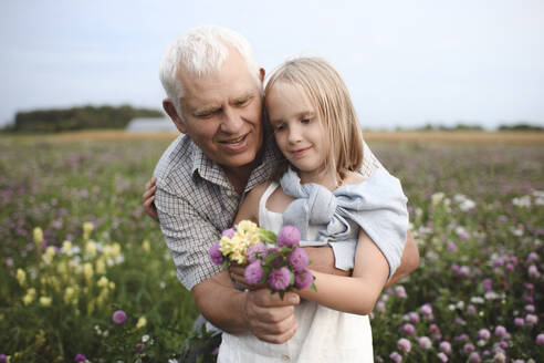 Porträt von Großvater und Enkelin mit gepflückten Blumen auf einer Wiese - EYAF00424