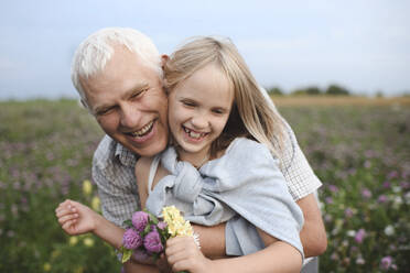 Porträt eines glücklichen Großvaters und einer Enkelin mit gepflückten Blumen auf einer Wiese - EYAF00425