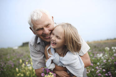 Lachender Großvater und Enkelin mit gepflückten Blumen auf einer Wiese - EYAF00427