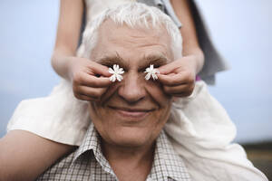 Hands of little girl covering eyes of her grandfather with white blossoms - EYAF00430