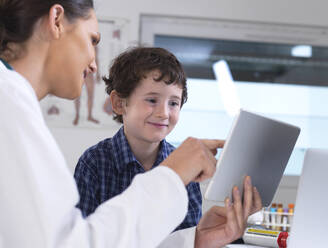 Eine Ärztin zeigt einem jungen männlichen Patienten seine Laborergebnisse auf einem digitalen Tablet in der Klinik - ABRF00577