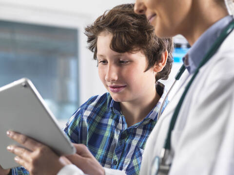 Eine Ärztin zeigt einem jungen männlichen Patienten seine Laborergebnisse auf einem digitalen Tablet in der Klinik, lizenzfreies Stockfoto