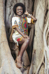 Lächelnde junge Frau posiert in einem Baumstamm - DLTSF00016