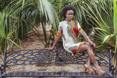 Junge Frau posiert auf einer Bank zwischen tropischen Pflanzen - DLTSF00026
