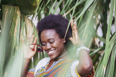 Smiling young woman standing among tropical plants - DLTSF00029