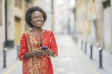 Lachende junge Frau, die mit ihrem Smartphone mitten auf einer Straße steht - DLTSF00040