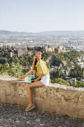 Junge Frau mit Kamera, die auf einer Mauer in der Alhambra sitzt, Granada, Spanien - LJF00957