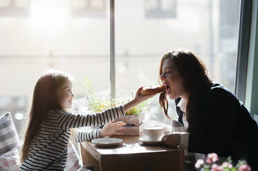 Lächelndes Mädchen, das ihrer Mutter in einem Café ein Stück Kuchen schenkt - EYAF00436