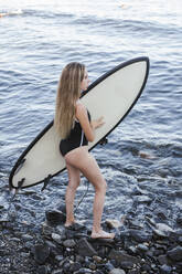 Weiblicher Teenager mit Surfbrett am steinigen Strand - LJF00967