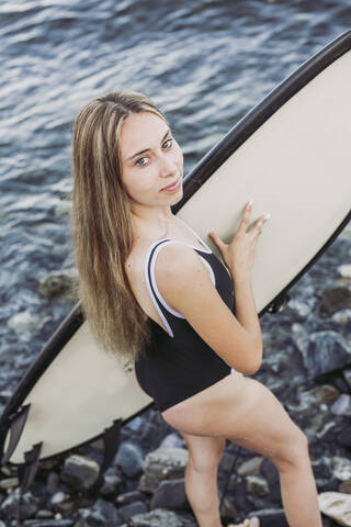 Weiblicher Teenager mit Surfbrett am steinigen Strand, lizenzfreies Stockfoto