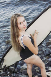 Weiblicher Teenager mit Surfbrett am steinigen Strand - LJF00968