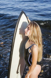 Weiblicher Teenager mit Surfbrett am steinigen Strand - LJF00973