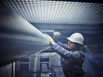 Handwerkerin mit Schutzhelm bei der Arbeit an einem Rohr - CVF01463