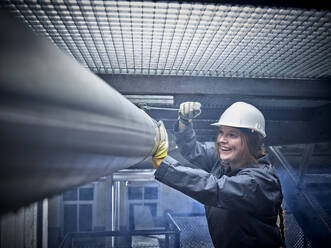 Glückliche Handwerkerin mit Schutzhelm bei der Arbeit an einem Rohr - CVF01464