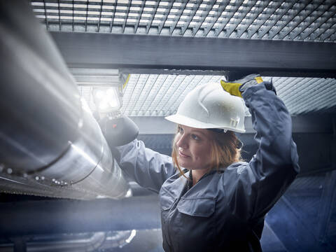 Handwerkerin mit Schutzhelm bei der Arbeit an einem Rohr, lizenzfreies Stockfoto