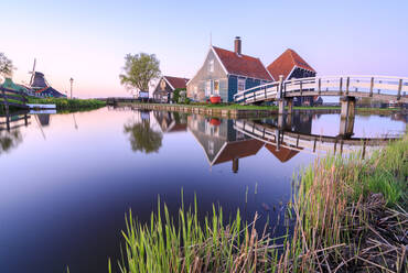 Holzhäuser und Windmühle spiegeln sich im blauen Fluss Zaan bei Sonnenuntergang, Zaanse Schans, Nordholland, Niederlande, Europa - RHPLF07771