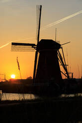 Silhouette einer typischen Windmühle, umrahmt von einem feurigen Himmel bei Sonnenuntergang, Kinderdijk, UNESCO-Weltkulturerbe, Molenwaard, Südholland, Niederlande, Europa - RHPLF07812