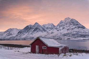 Rosa Wolken in der Morgendämmerung auf der Holzhütte, umgeben von gefrorenem Meer und verschneiten Gipfeln, Svensby, Lyngen Alps, Troms, Norwegen, Skandinavien, Europa - RHPLF07952