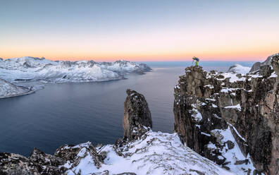 Fotograf auf den Felsen des Berges Hesten bewundert den Mefjorden und das gefrorene Meer bei Sonnenaufgang, Senja, Troms, Norwegen, Skandinavien, Europa - RHPLF07971