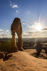 Delicate Arch mit Sonne und Wolken zur goldenen Stunde, Arches National Park, Moab, Grand County, Utah, Vereinigte Staaten von Amerika, Nordamerika - RHPLF08120