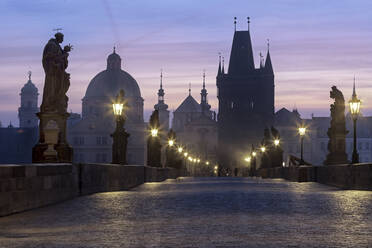 Straßenlaternen und alte Statuen umrahmen die historischen Gebäude auf der Karlsbrücke in der Morgendämmerung, UNESCO-Weltkulturerbe, Prag, Tschechische Republik, Europa - RHPLF08273