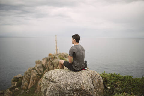 Trailrunner auf einem Felsen in Küstenlandschaft sitzend, Ferrol, Spanien, lizenzfreies Stockfoto