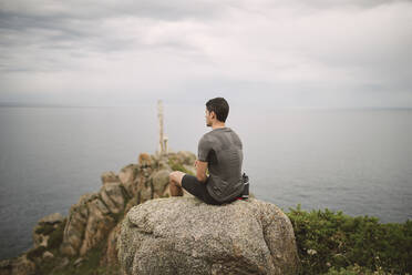 Trailrunner auf einem Felsen in Küstenlandschaft sitzend, Ferrol, Spanien - RAEF02286