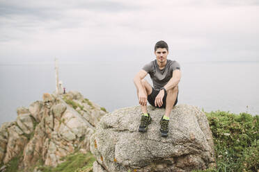 Porträt eines Trailrunners, der auf einem Felsen in einer Küstenlandschaft sitzt, Ferrol, Spanien - RAEF02287