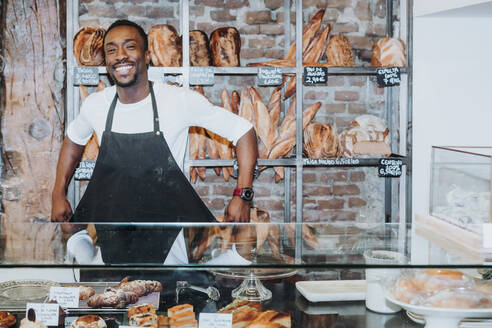 Lächelnder Mann, der in einer Bäckerei arbeitet und seine Schürze auszieht - JCMF00150